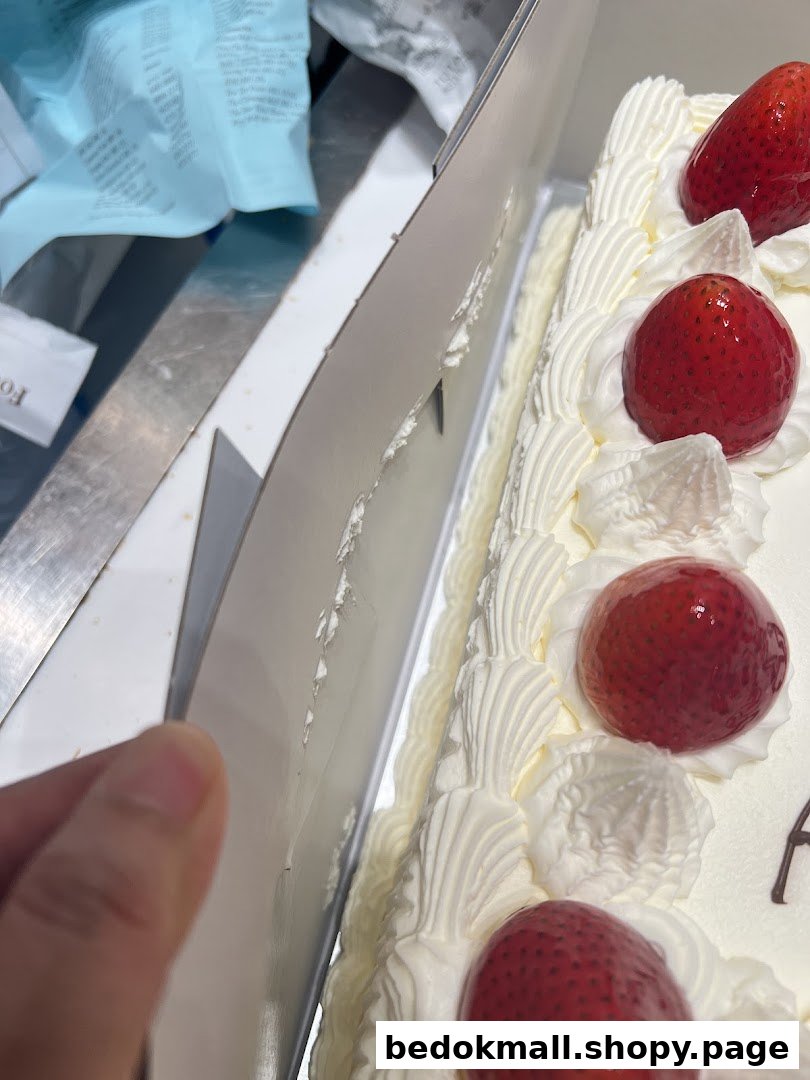 Close-up of a strawberry cake in a box, held by a hand.