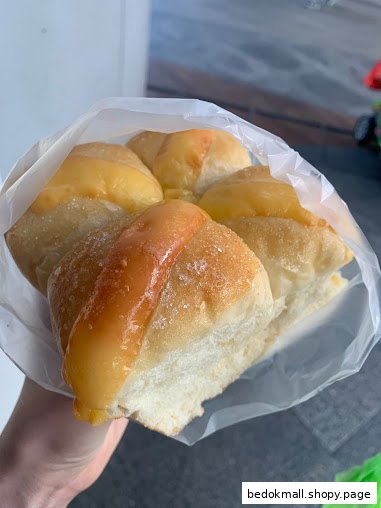Hand holding a plastic bag of sweet, glazed bread rolls.