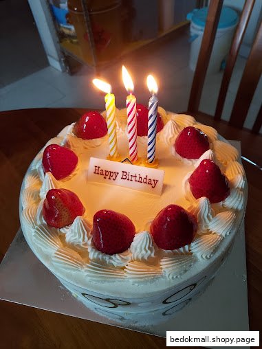 A birthday cake with lit candles, strawberries, and a 'Happy Birthday' sign.