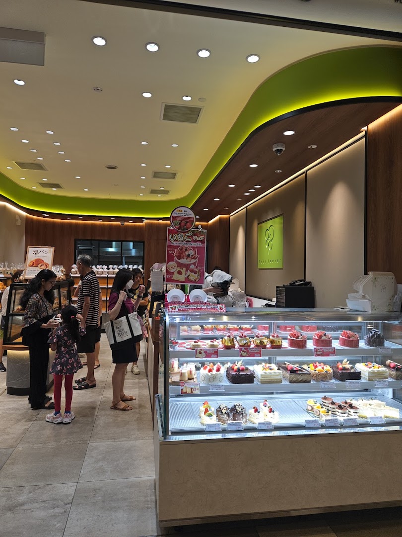 Bakery interior with customers, staff, and a display case full of cakes.