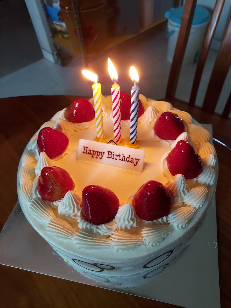 A white birthday cake with lit candles, strawberries, and a 'Happy Birthday' sign.