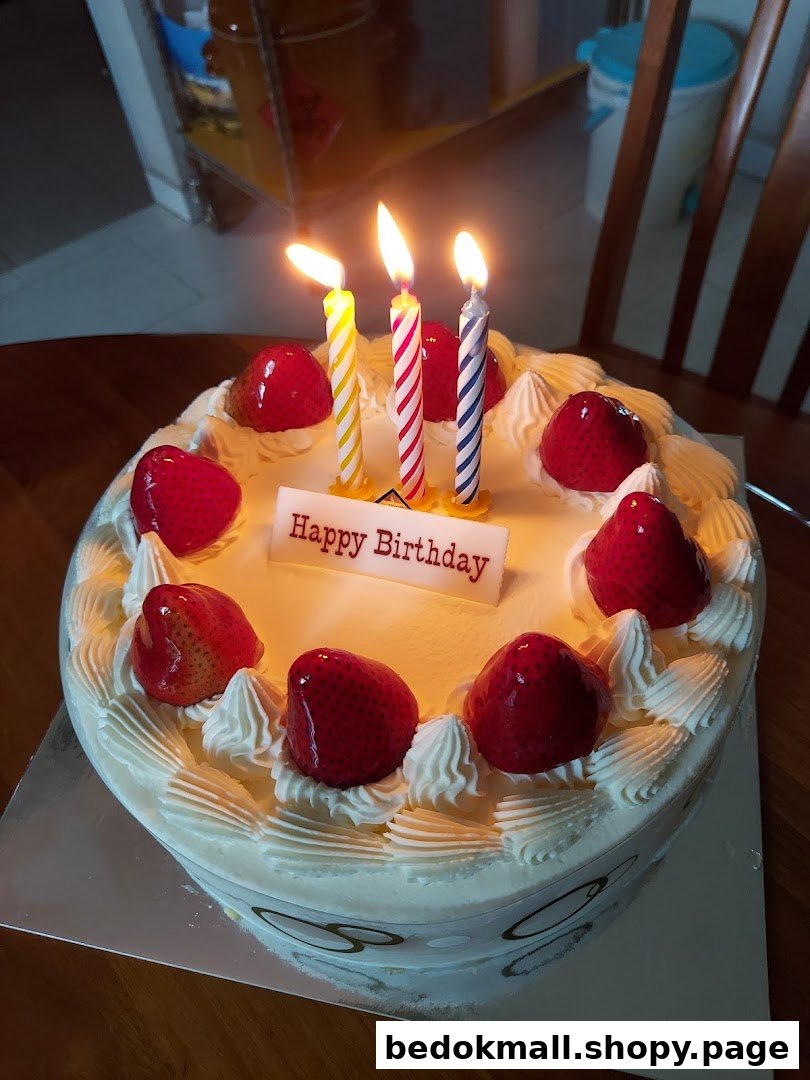 A white birthday cake with lit candles, strawberries, and a 'Happy Birthday' sign.
