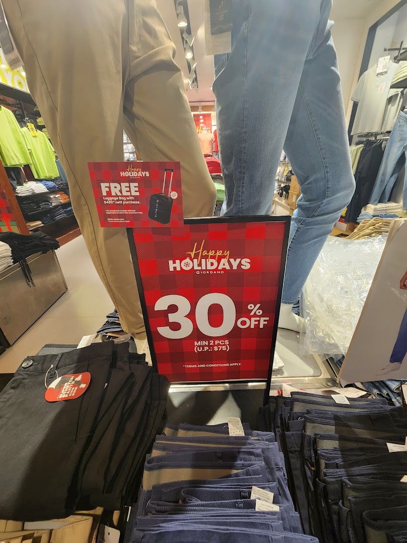 Mannequins and folded clothing with holiday sale signs inside a retail store.