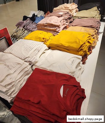 Stacks of folded t-shirts in various colors displayed on a table inside a clothing store.