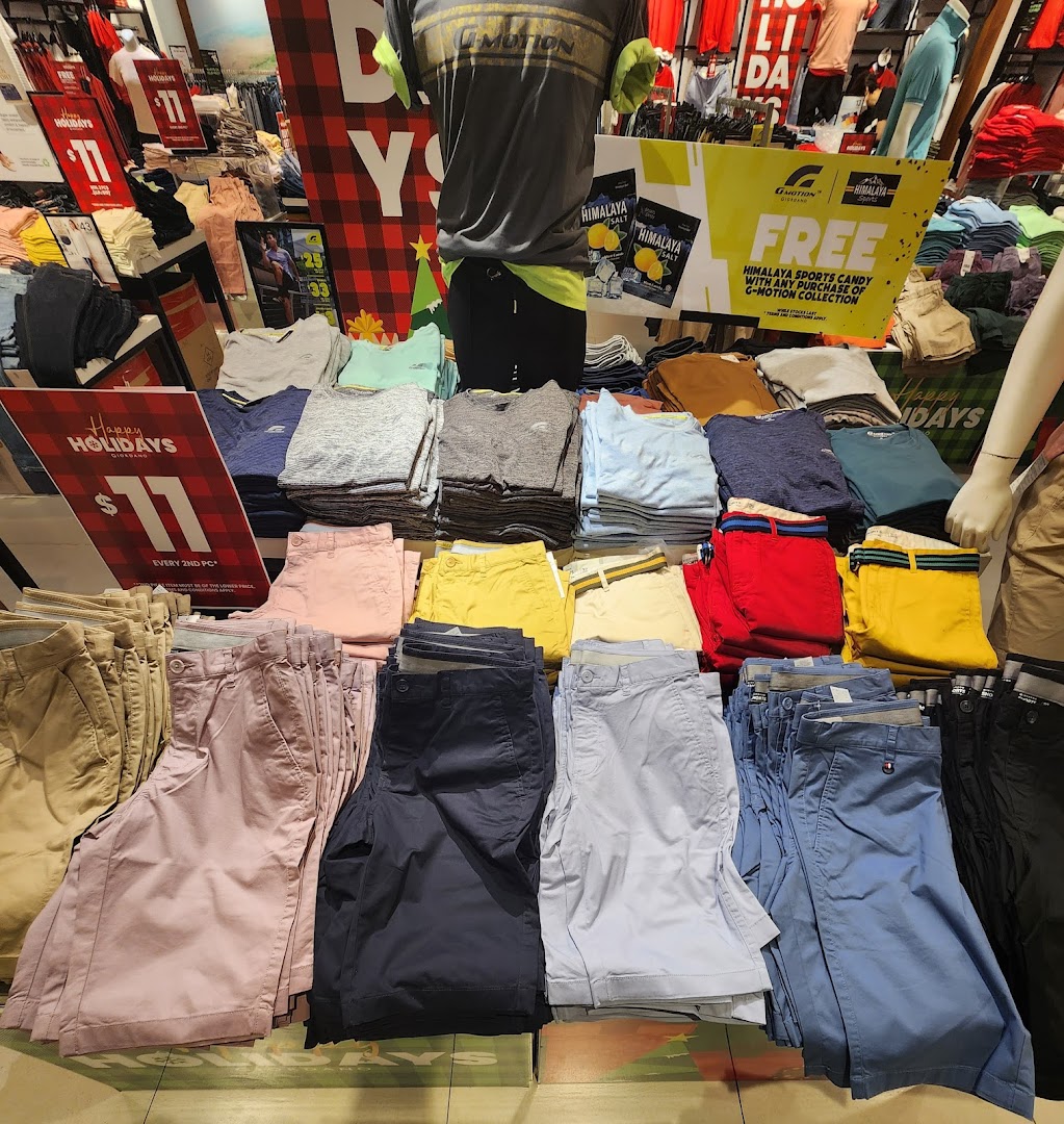 Interior view of a clothing store with folded apparel and promotional signs.