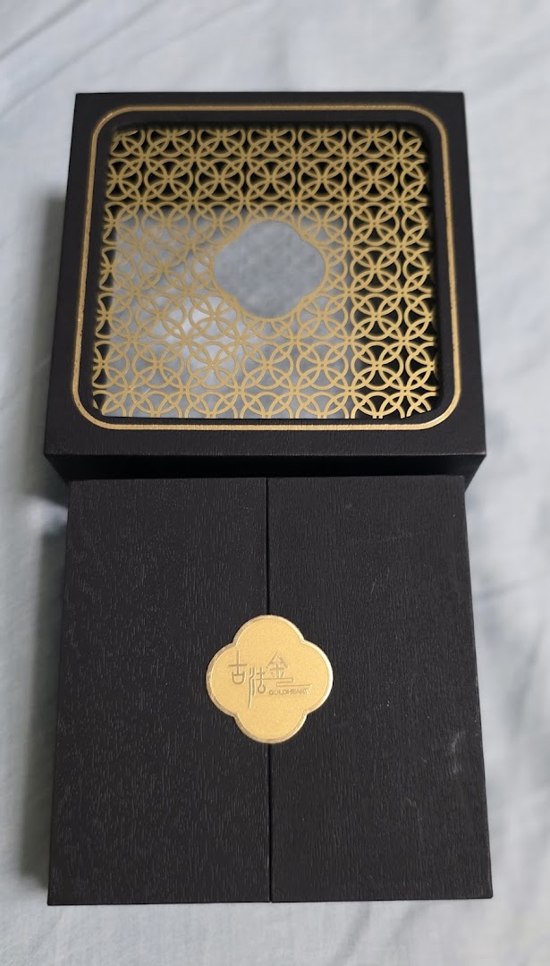 A black gift box with a gold patterned lid and a gold logo.