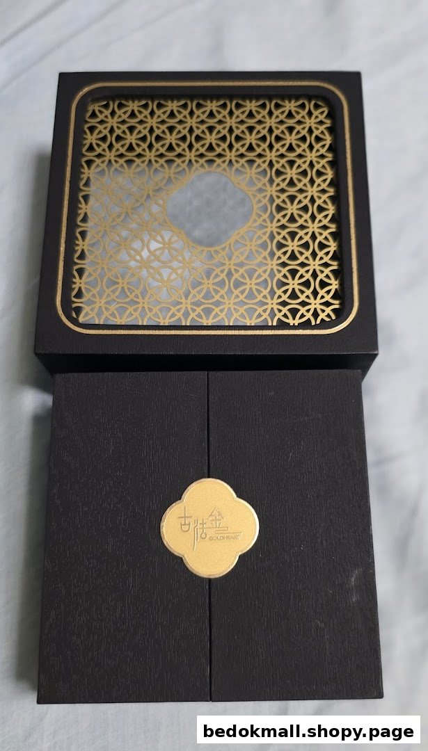 A black gift box with a gold patterned lid and a gold logo.
