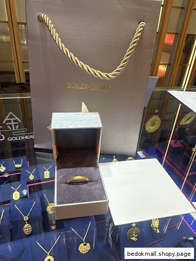 Gold ring in an open box with a Goldheart shopping bag and jewelry display.