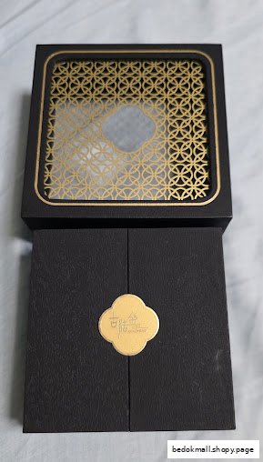 A black jewelry box with a gold patterned lid and a gold emblem.