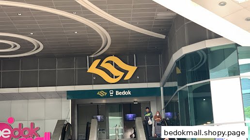 Exterior view of Bedok MRT station entrance with escalators and mall signage.