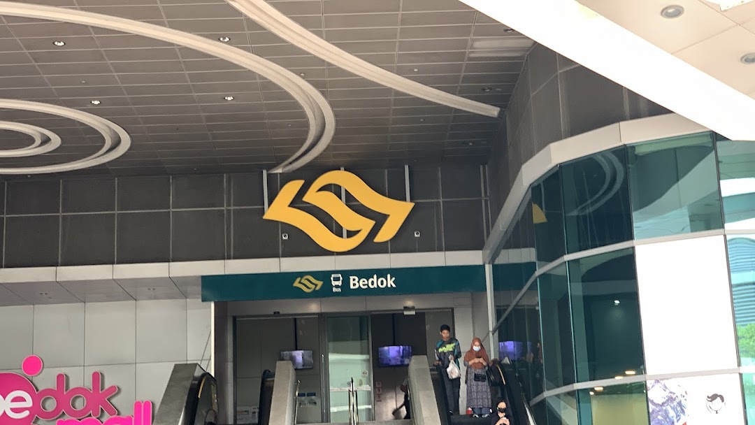 Entrance to Bedok transport hub with escalators and people.