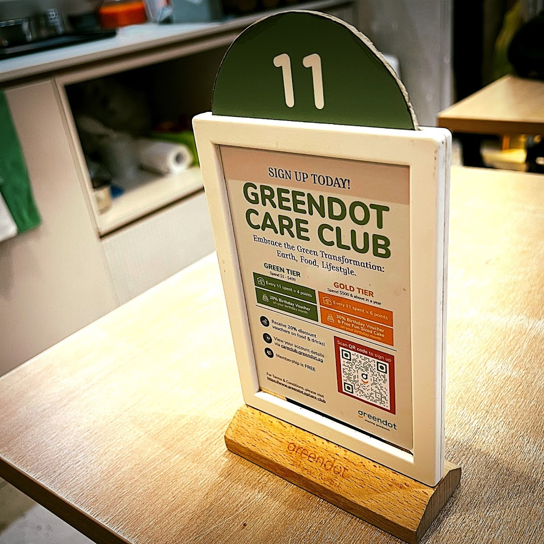 Table stand displaying Greendot Care Club loyalty program details with a QR code.