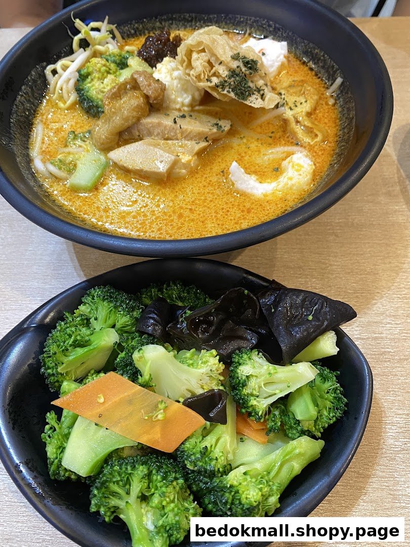 Two bowls of food: a noodle dish with broth and a side of broccoli.