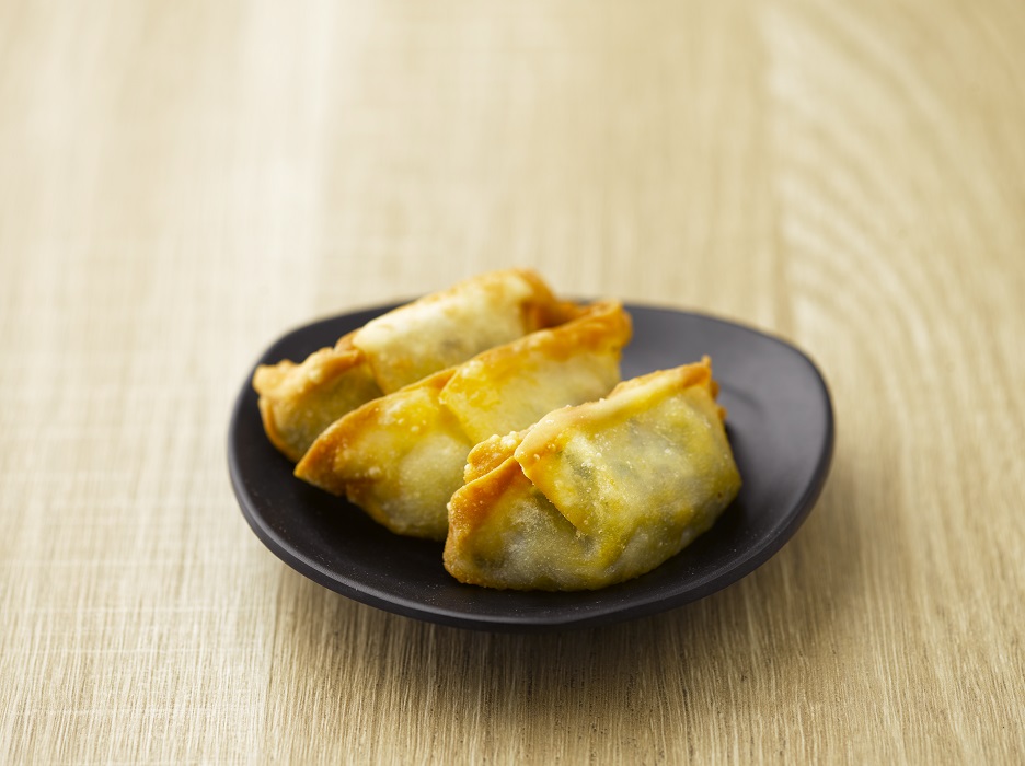 Four fried dumplings are served on a black plate on a wooden surface.