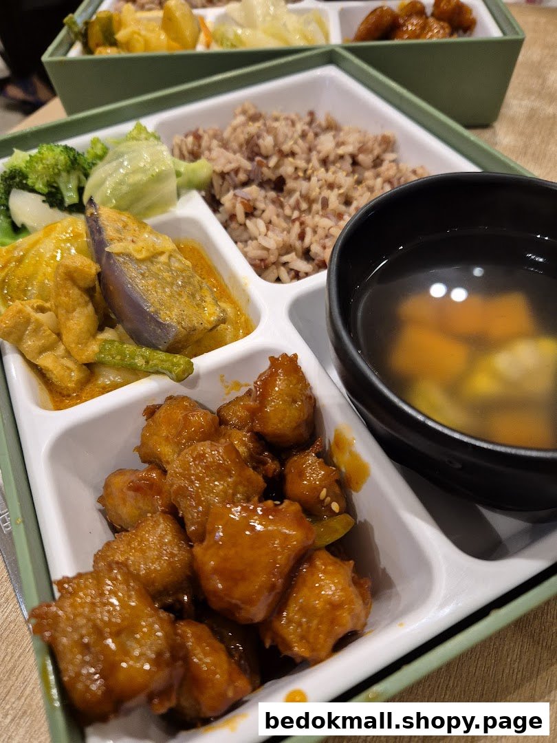 A bento box meal with rice, vegetables, nuggets, and soup.