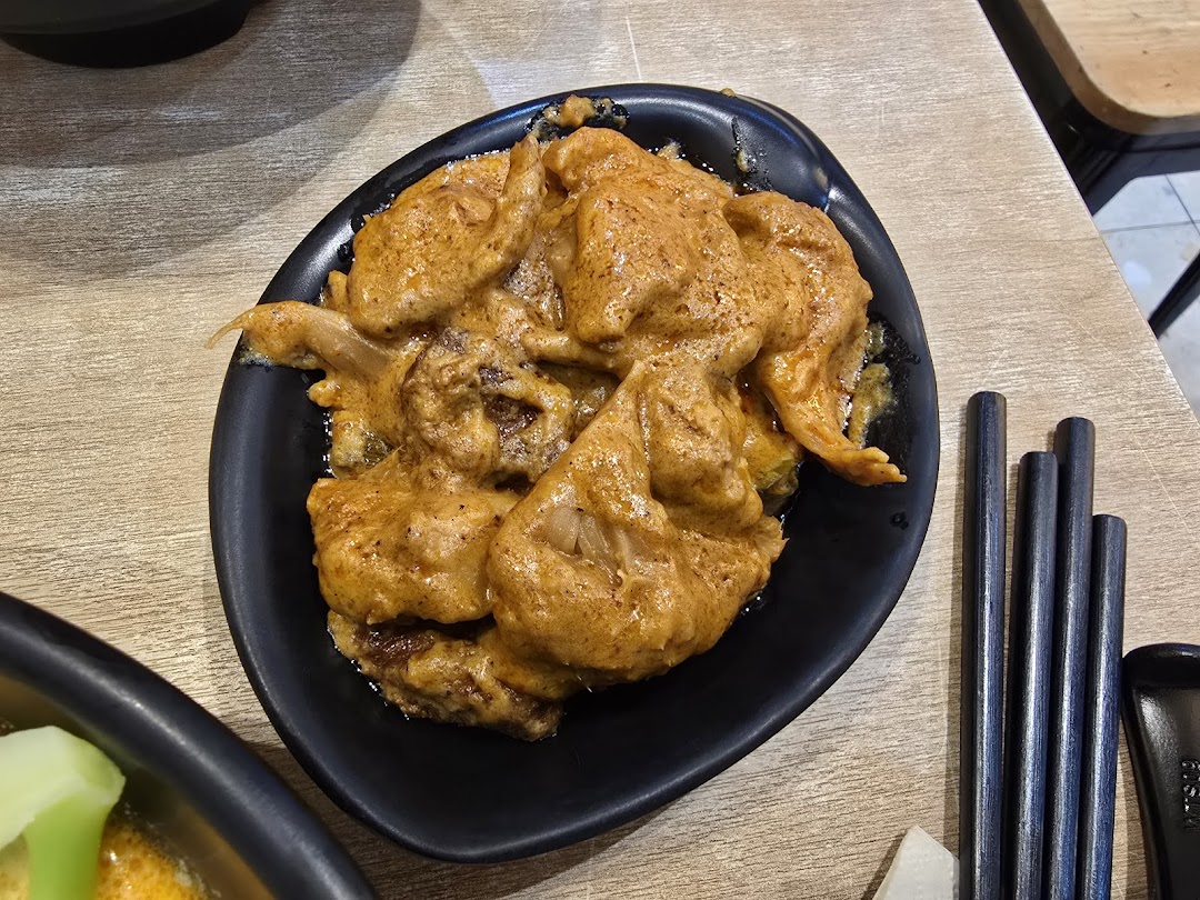 A dish with orange sauce in a black bowl on a wooden table with chopsticks.