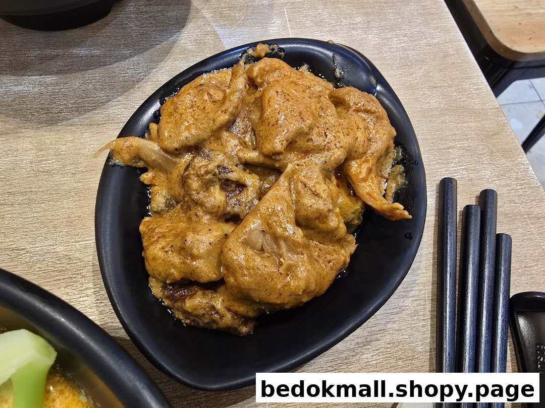 A dish with orange sauce in a black bowl on a wooden table with chopsticks.