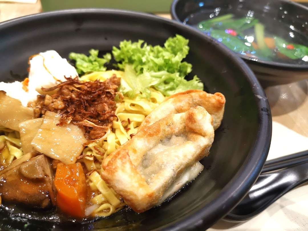 Close-up of a bowl of noodles with various toppings and a side of soup.