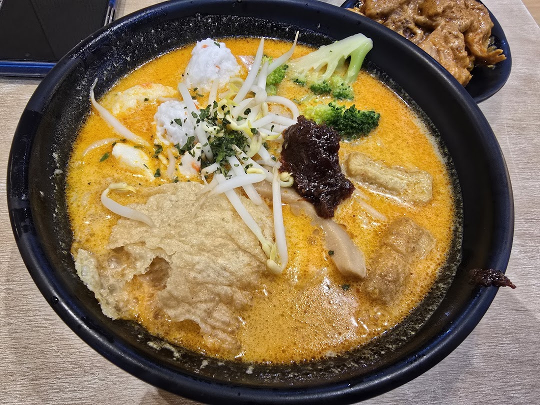 Close-up of a bowl of curry noodles with vegetables and tofu.
