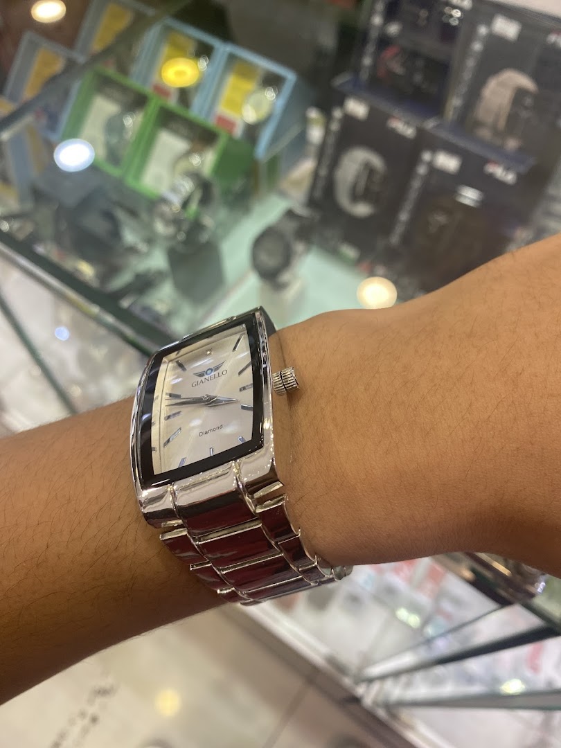 A person's arm wearing a watch, with blurred shop displays in the background.
