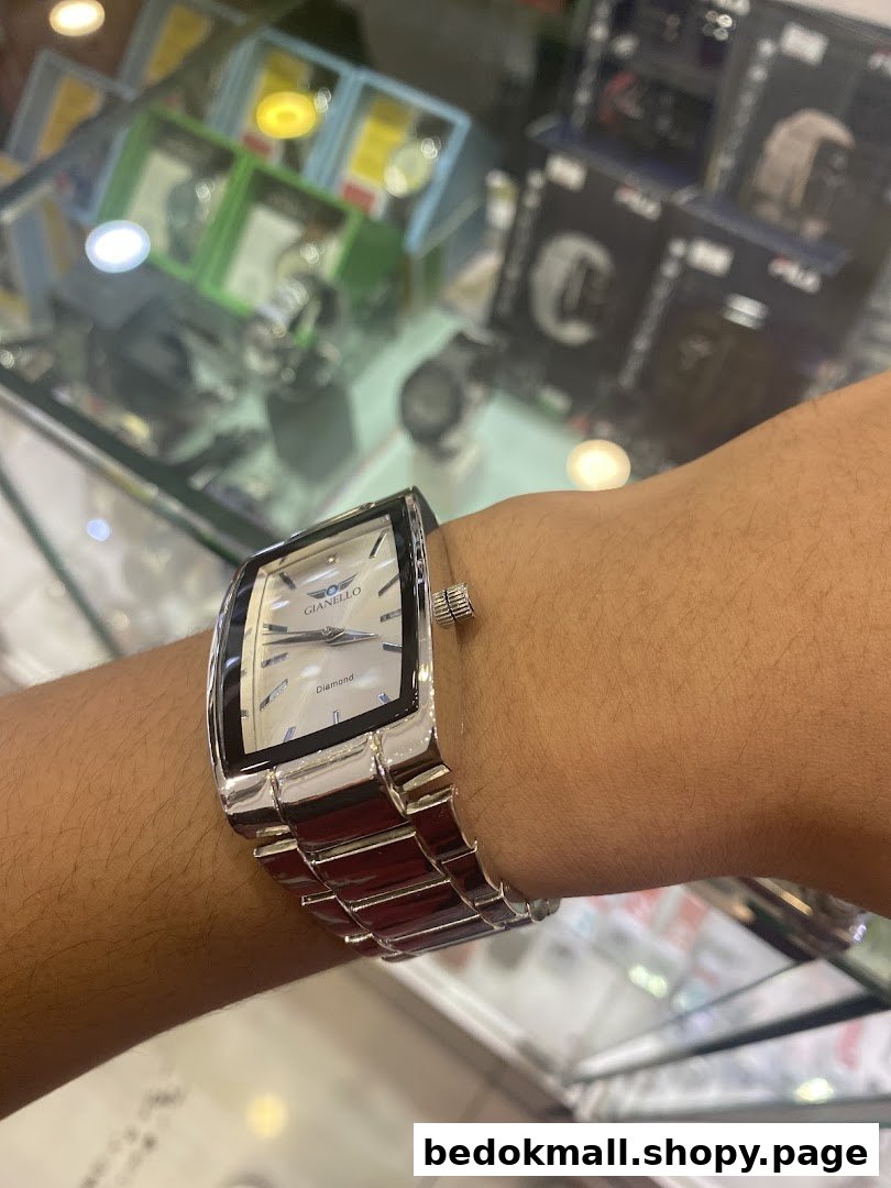 A person's arm wearing a watch, with blurred shop displays in the background.