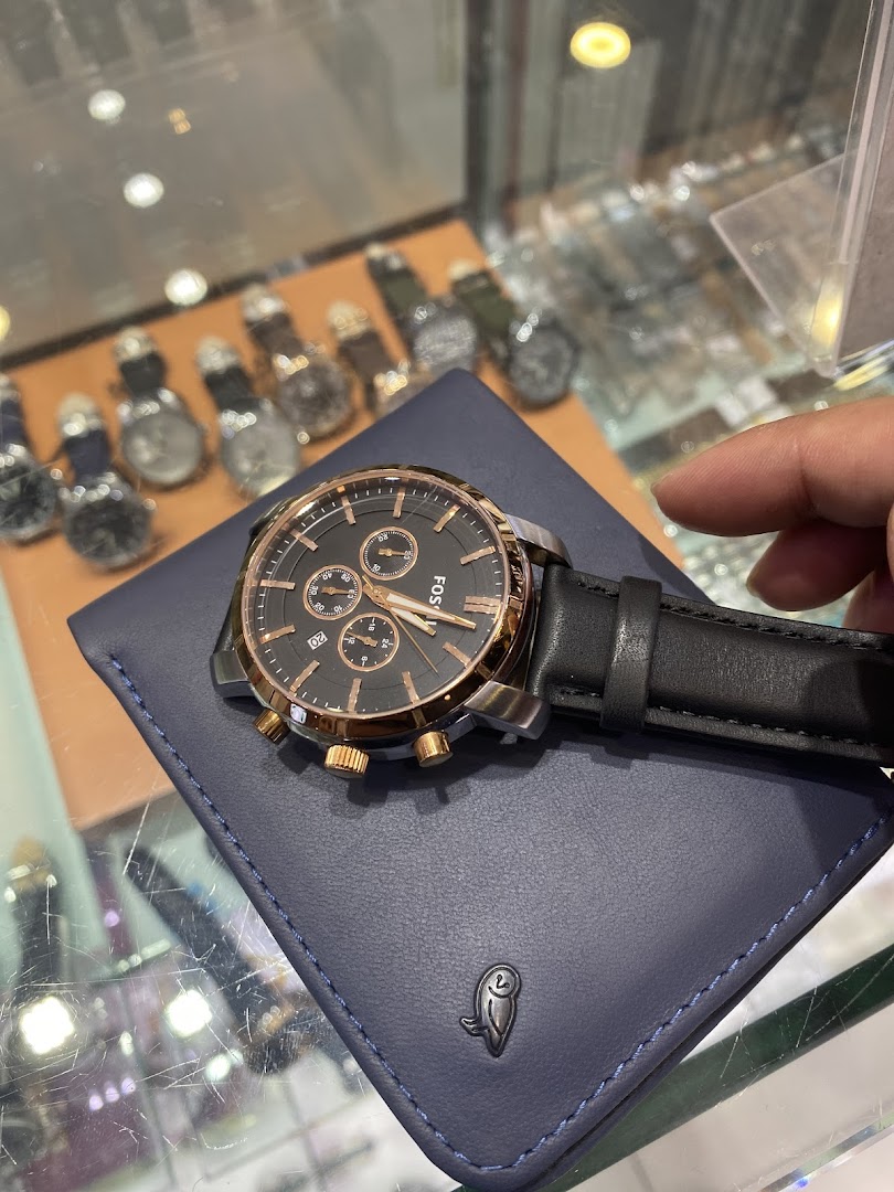 Close-up of a Fossil watch on a blue wallet, with other watches in background.