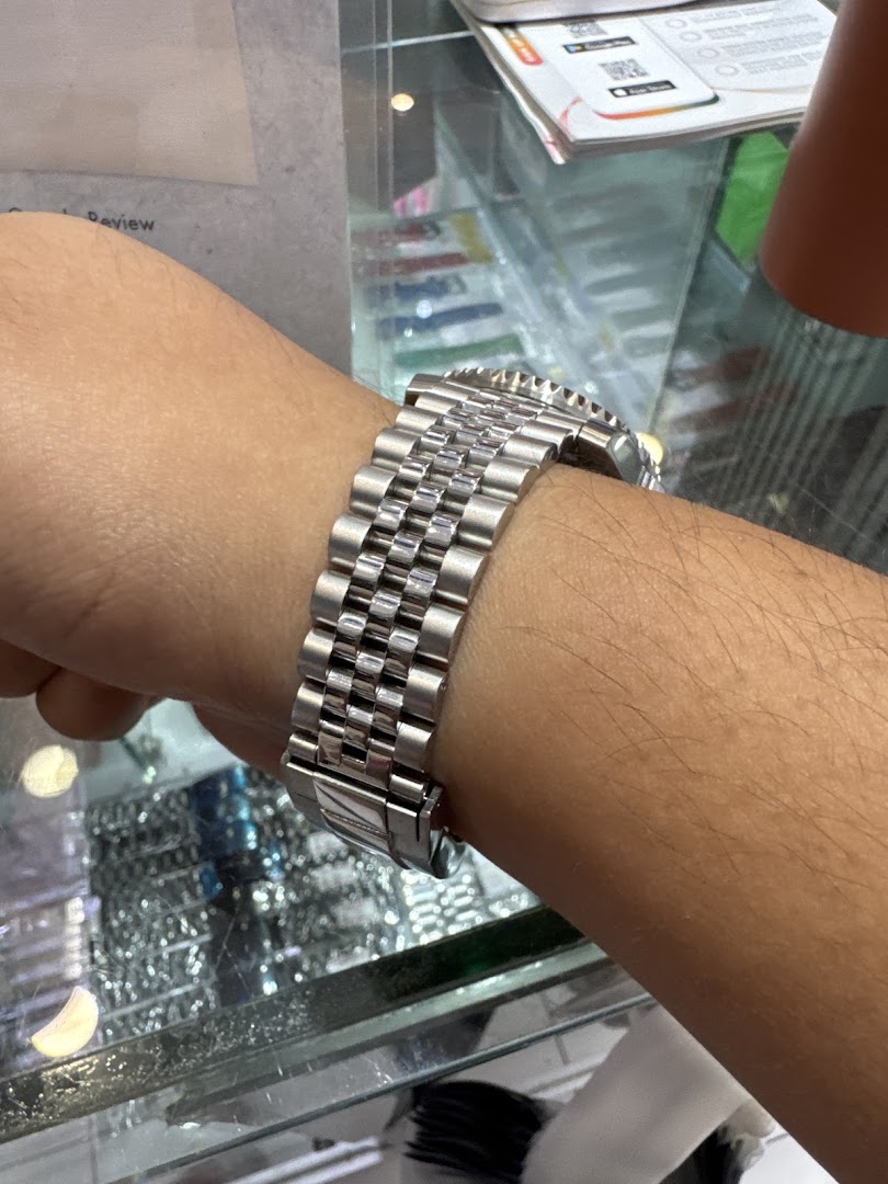 A person's arm wearing a watch, with a display case in the background.
