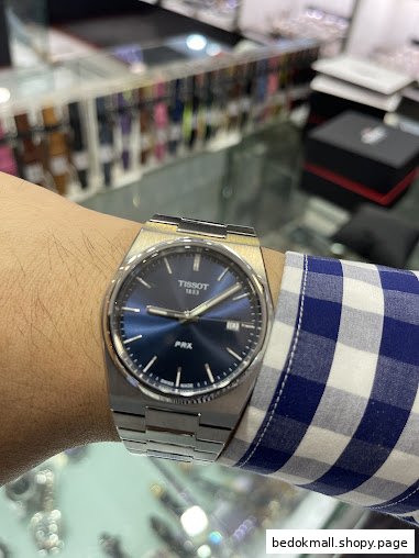 Person wearing a Tissot watch in a retail store with blurred displays.