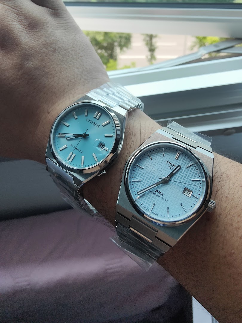 Two light blue dial watches, Citizen and Tissot, on a person's arm.