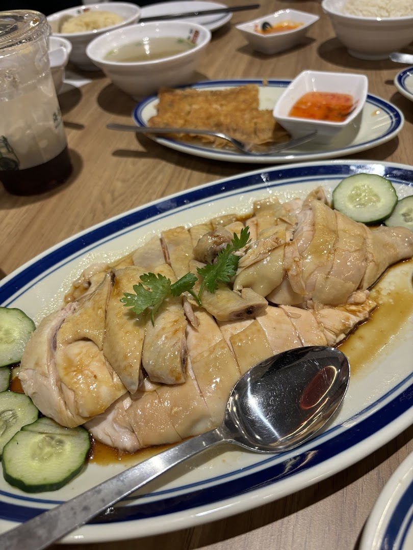 A plate of Hainanese chicken with other dishes on a wooden table.