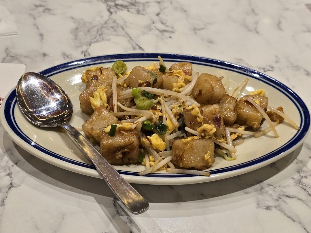 A plate of fried radish cake with bean sprouts and egg on a marble table.