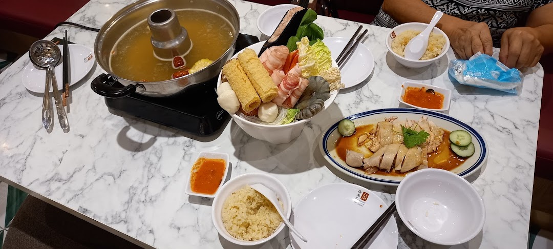 A table with hotpot, various ingredients, Hainanese chicken, and rice.