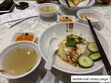 Hainanese chicken rice meal with soup and sauces on a marble table.
