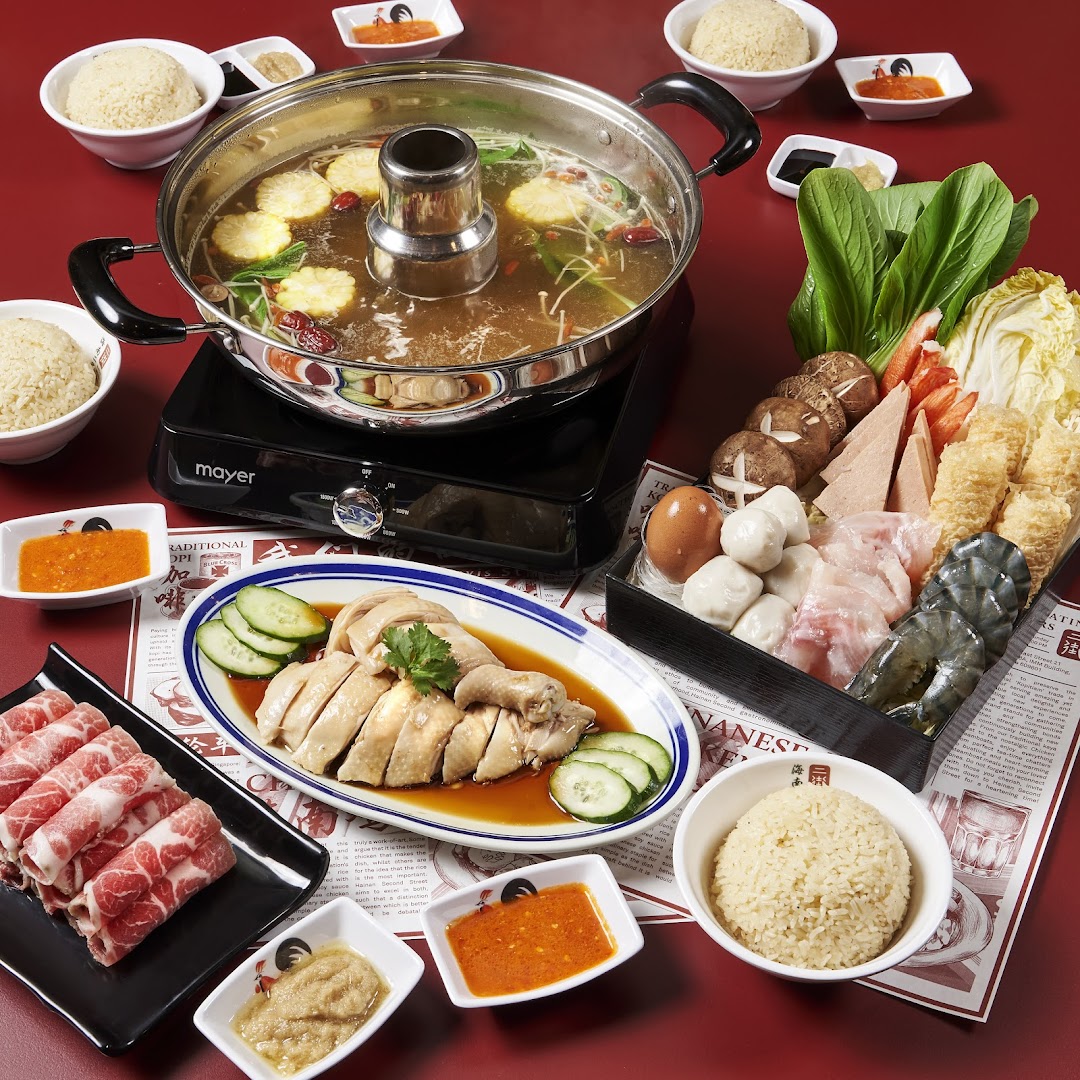 A spread of hot pot, chicken rice, and various ingredients on a red table.