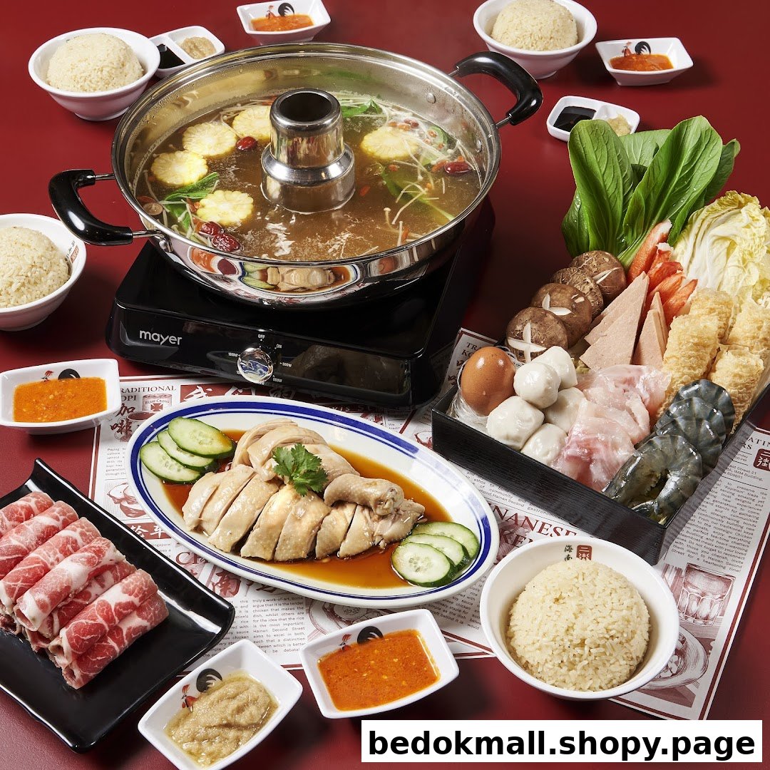 A spread of hot pot, chicken rice, and various ingredients on a red table.