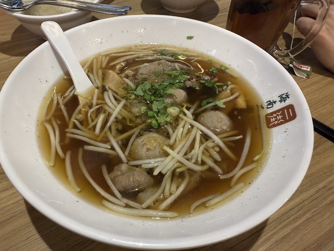 A close-up of a bowl of noodles with meat and sprouts in soup.
