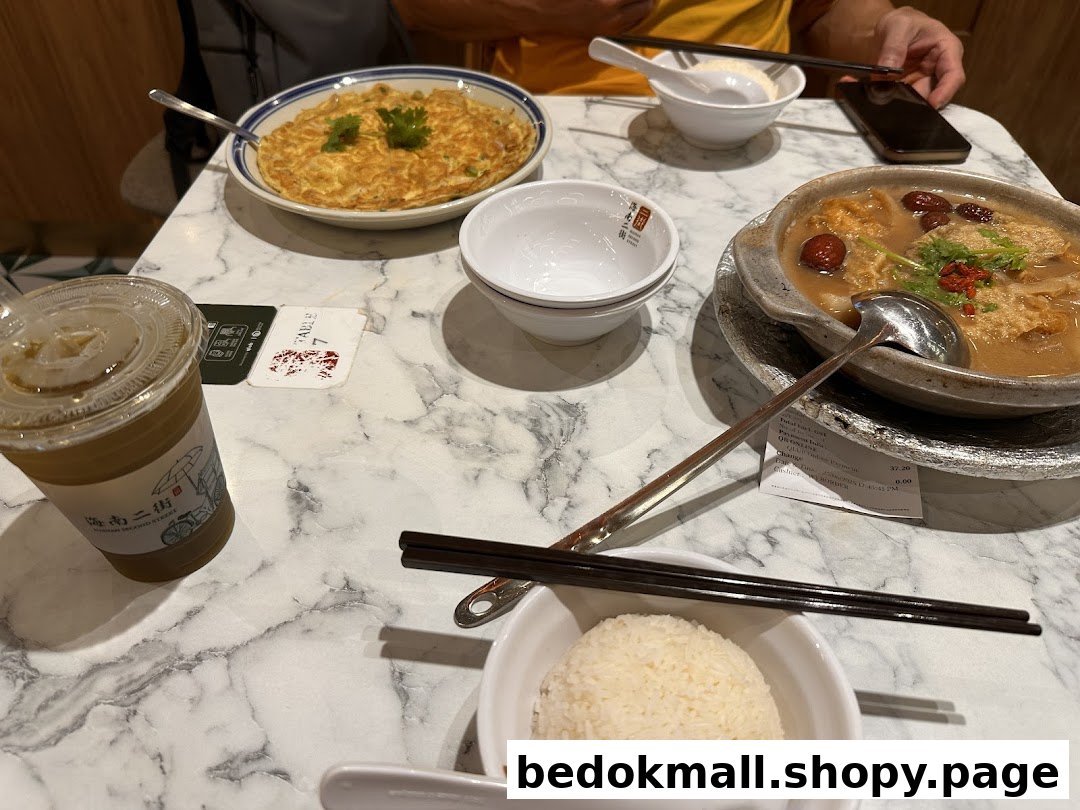 A table with various dishes, drinks, and a person's hands in a restaurant setting.