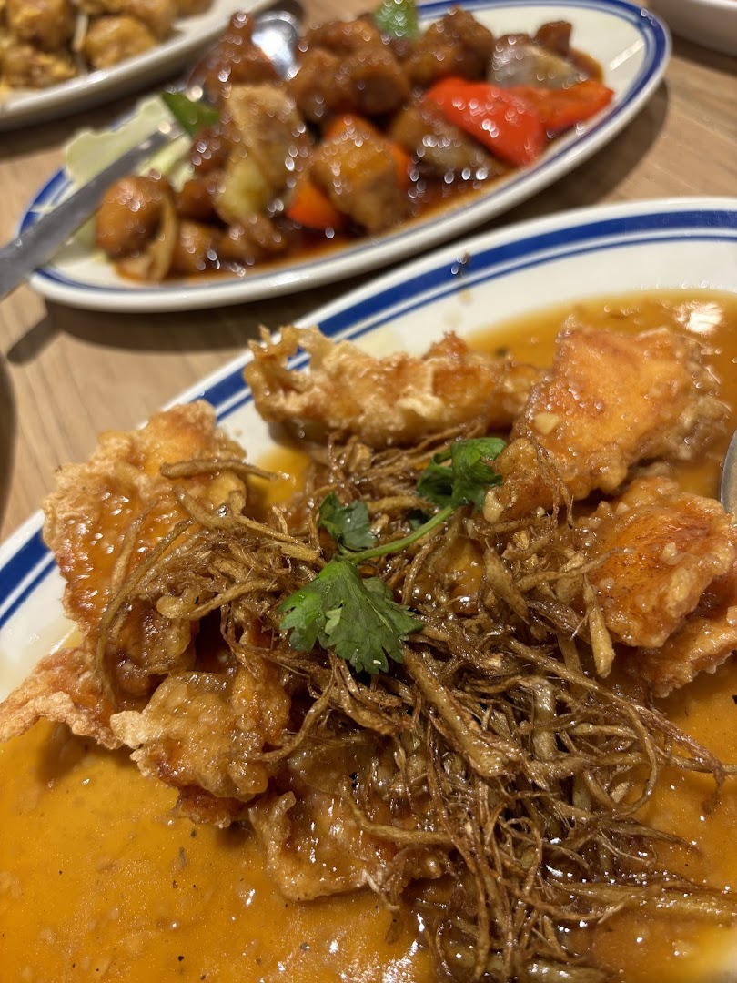 Two plates of Asian food, including fried fish with sauce, on a table.