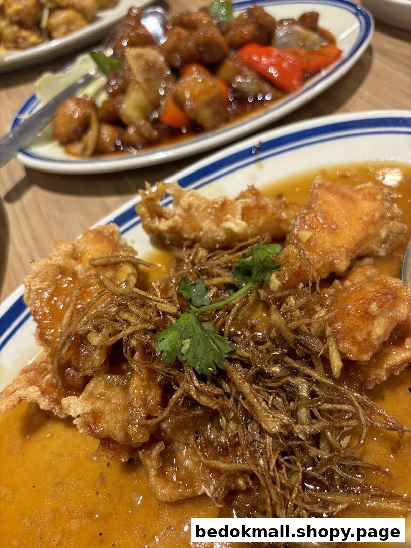 Two plates of Asian food, including fried fish with sauce, on a table.