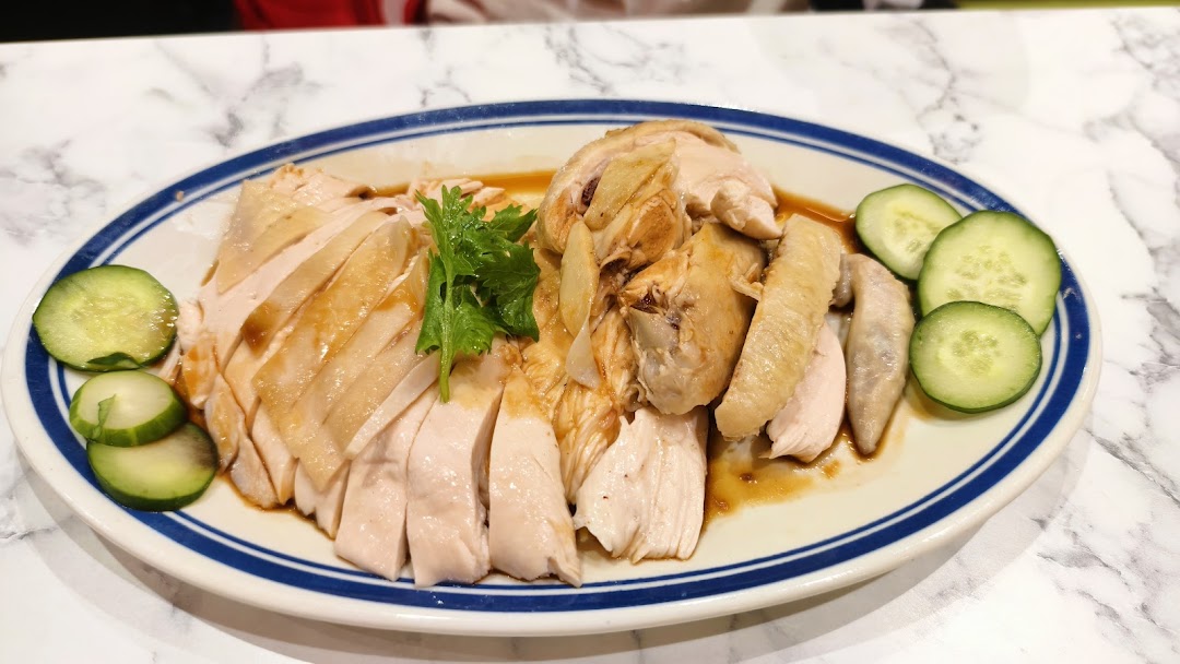 A plate of sliced Hainanese chicken with cucumber slices on a marble table.