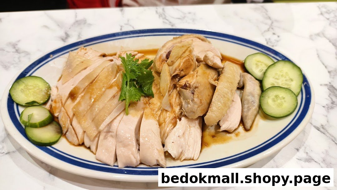A plate of sliced Hainanese chicken with cucumber slices on a marble table.