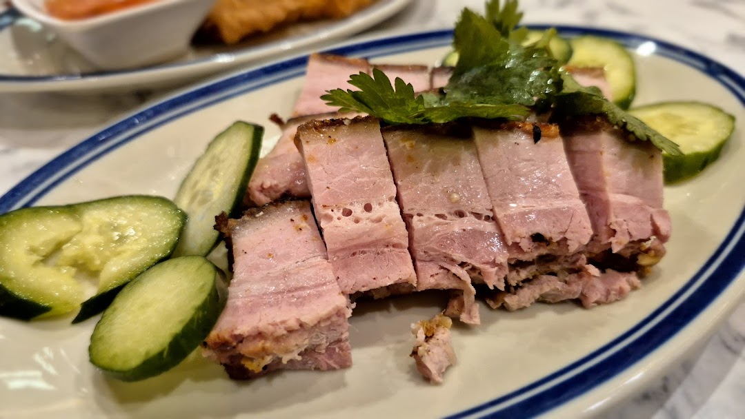 Close-up of sliced pork belly with cucumber and herbs on a plate.