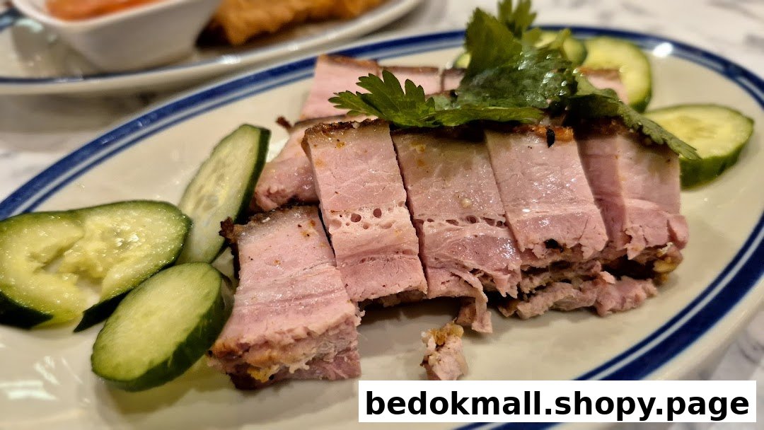 Close-up of sliced pork belly with cucumber and herbs on a plate.