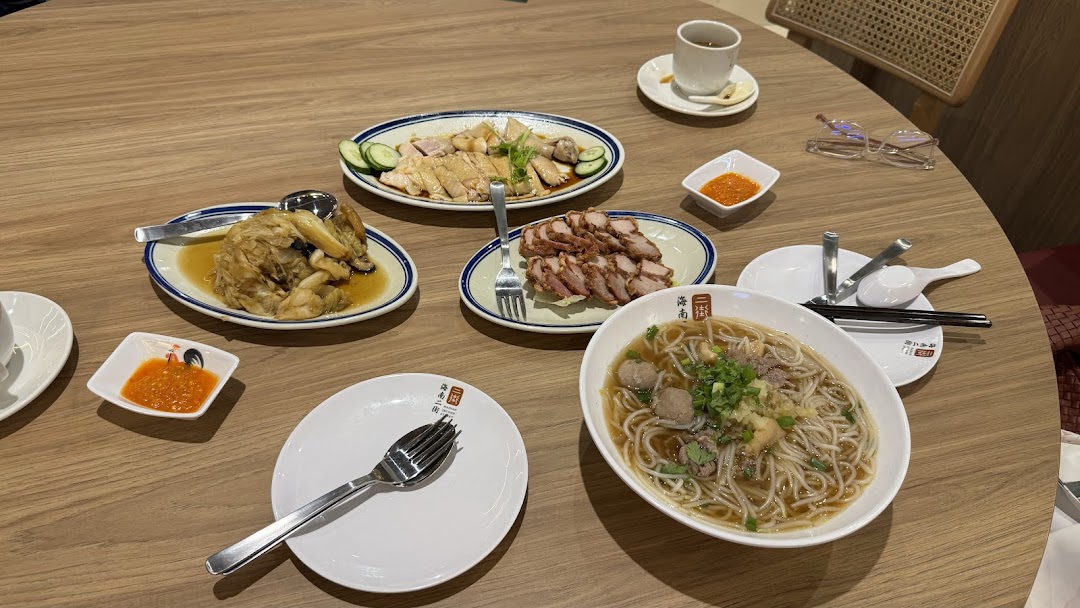 Table with multiple dishes of Hainanese food, including chicken, char siu, and noodles.