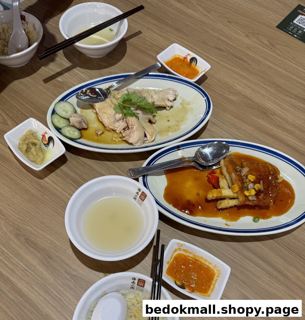 Dishes of Hainanese chicken rice and other food on a wooden table.
