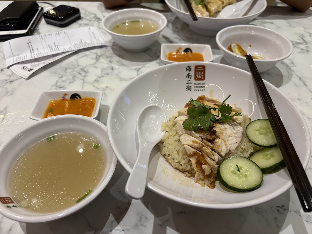 A table with Hainanese chicken rice, soup, and condiments in a restaurant.