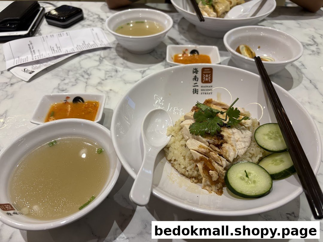 A table with Hainanese chicken rice, soup, and condiments in a restaurant.