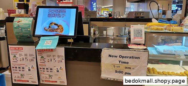 Shop counter with display screen, food items, and operation time sign.