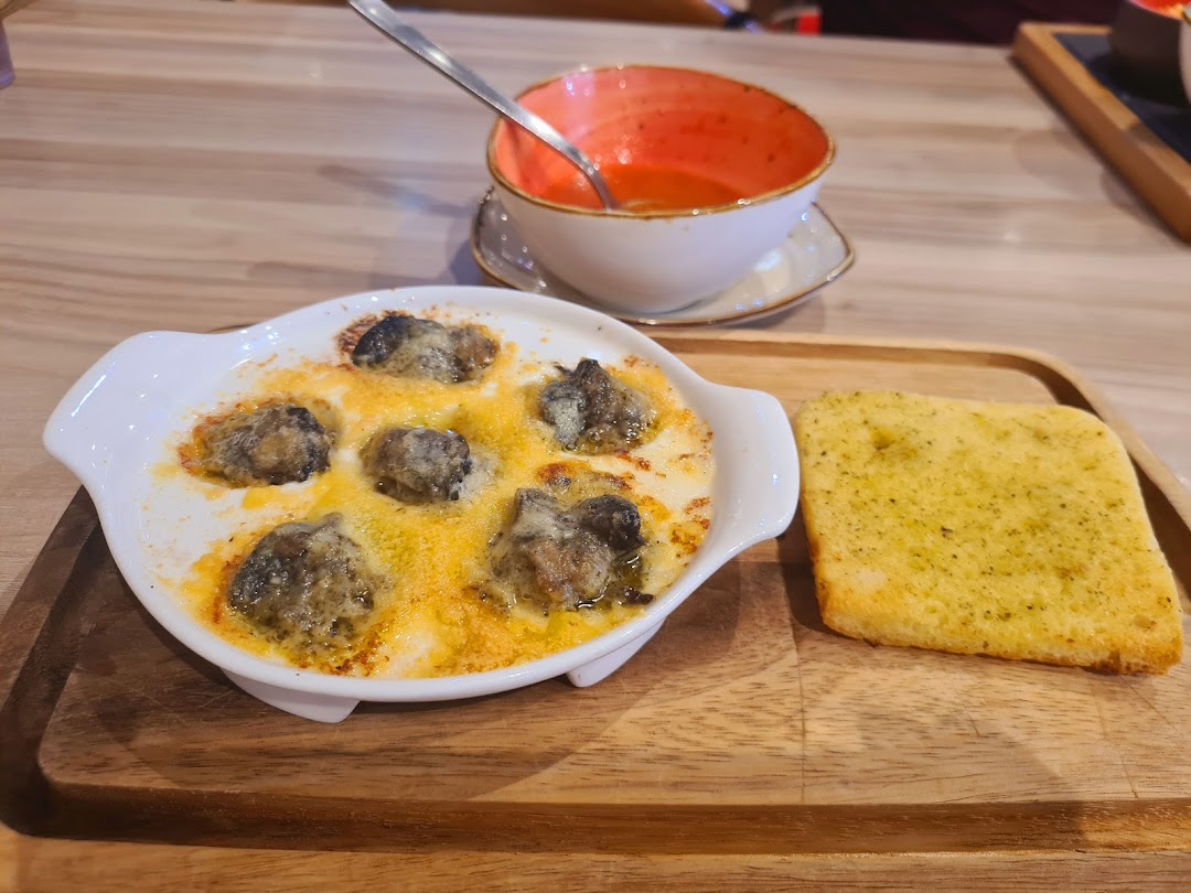 A dish of escargots, garlic bread, and soup on a wooden tray.