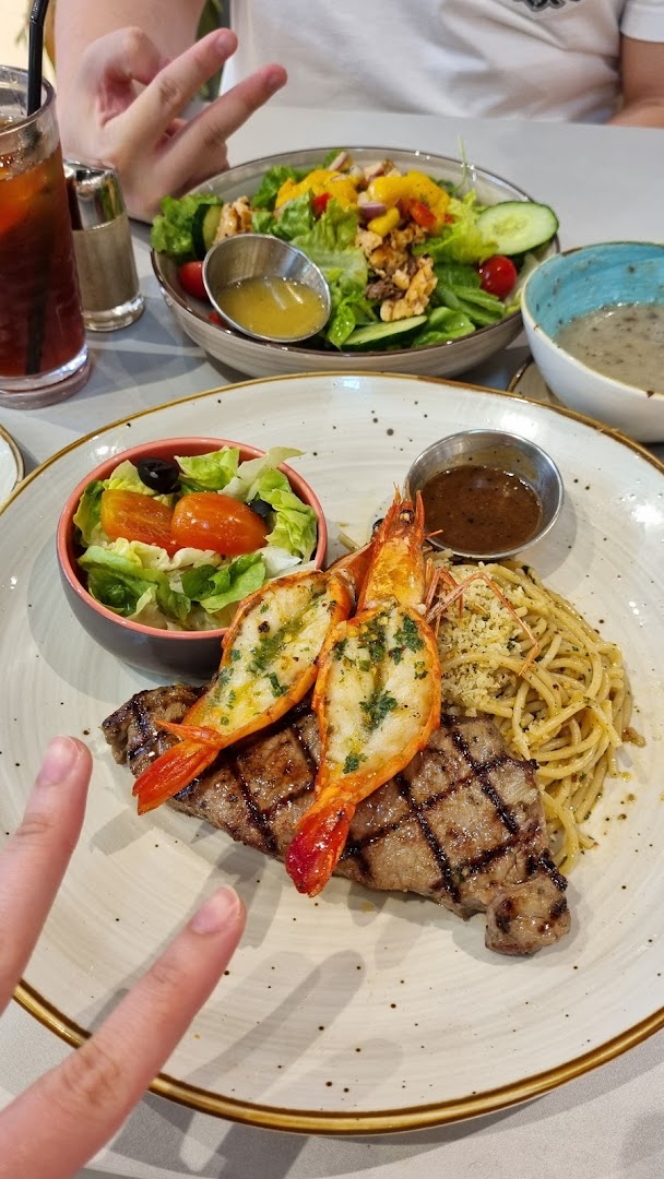 A plate of grilled steak and prawns with pasta and salad on a table.